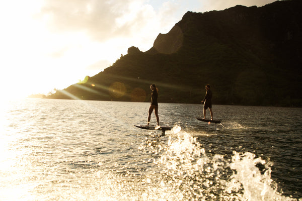 Two riders gliding across the ocean on their eFoils during a sunset